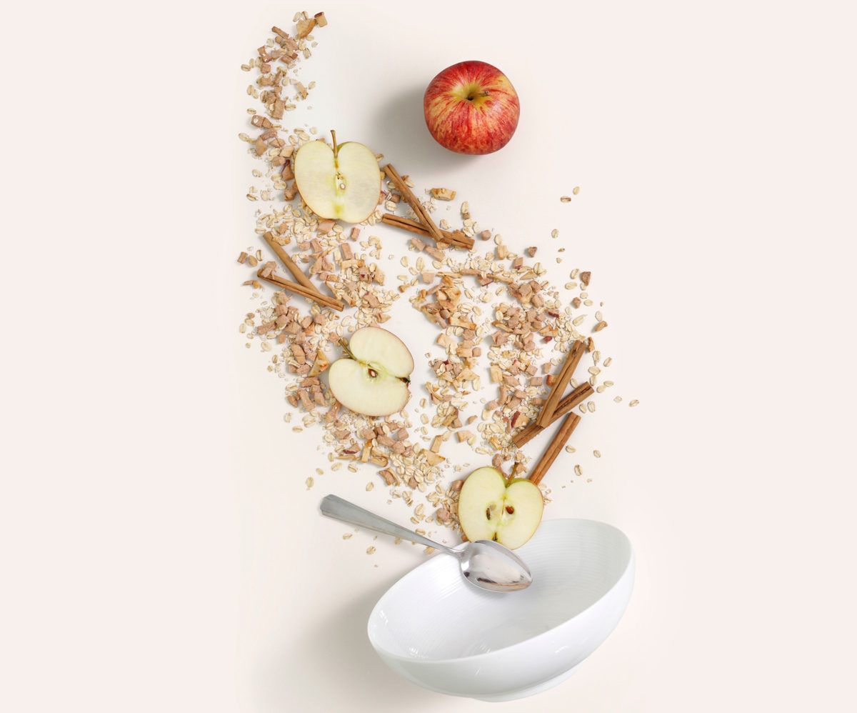 Schwebendes Muesli mit Apfelscheiben und Zimtstangen faellt in eine weisse Schale — Das Studiozwei, Werbefotograf München