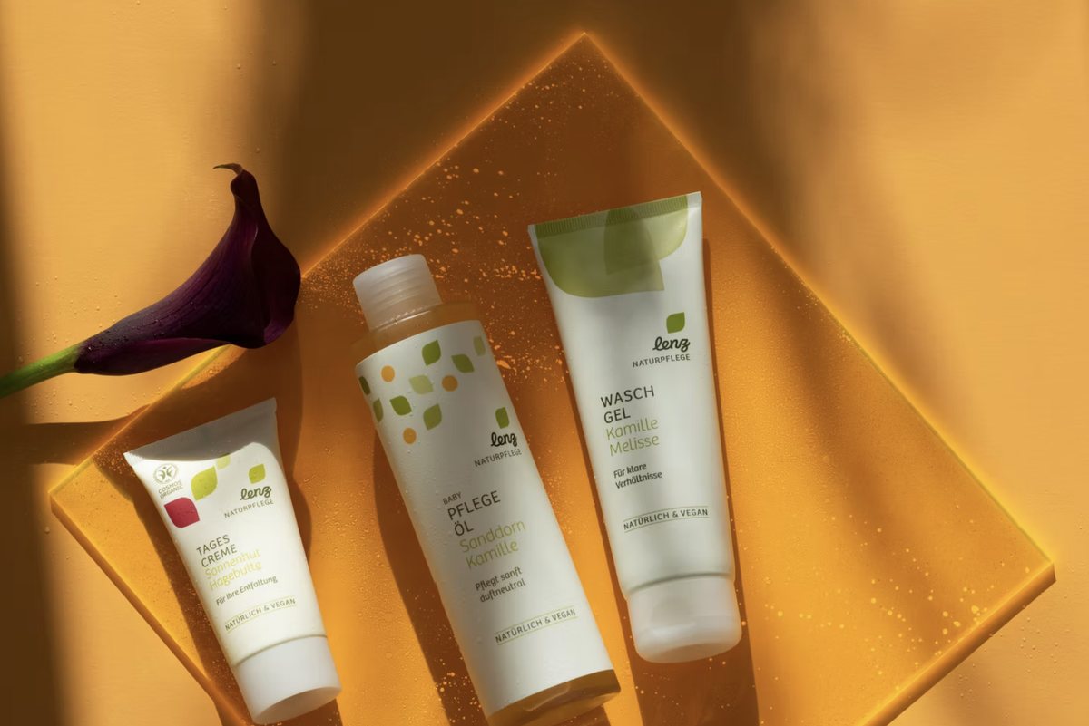 Drei Naturkosmetik-Produkte auf oranger Acrylplatte mit Calla-Bluete, Aufsicht — Das Studiozwei, Werbefotograf München