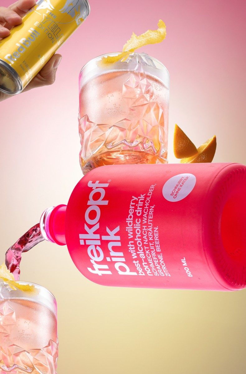 Schwebende pinke Flasche mit rosa Drinks, Eis und Zitrusfilets vor rosa-gelbem Verlauf — Das Studiozwei, Werbefotograf München