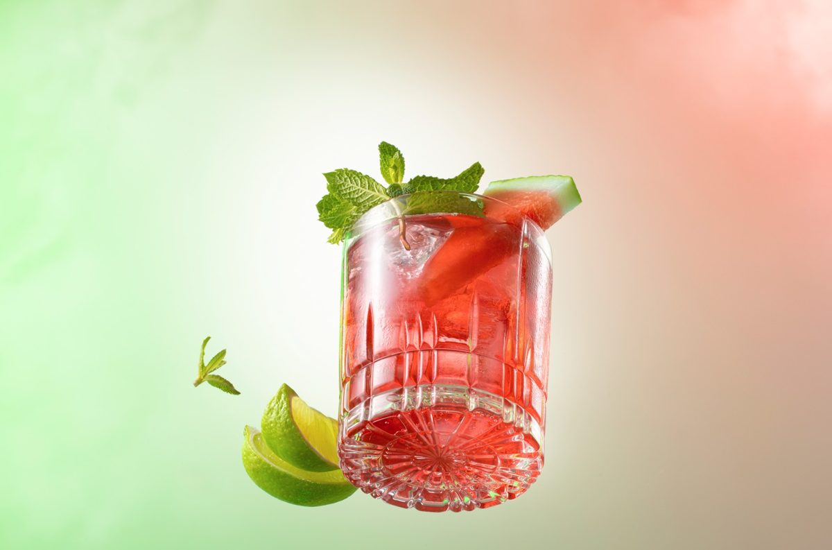 Schwebendes Glas mit rotem Drink, Minze, Melone und Limette vor gruen-rosa Verlauf — Das Studiozwei, Werbefotograf München
