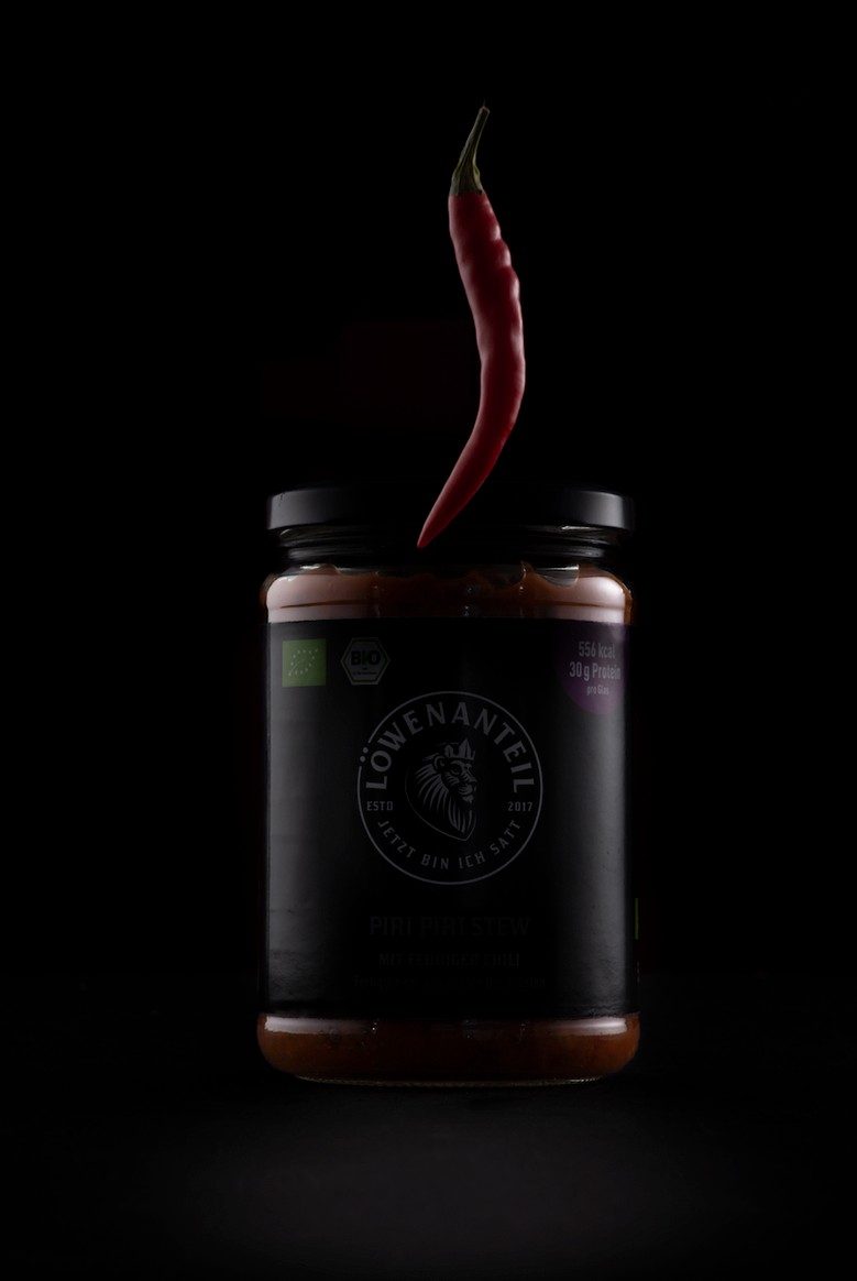 Dunkles Saucenglas mit schwebender roter Chilischote vor schwarzem Hintergrund — Das Studiozwei, Werbefotograf München