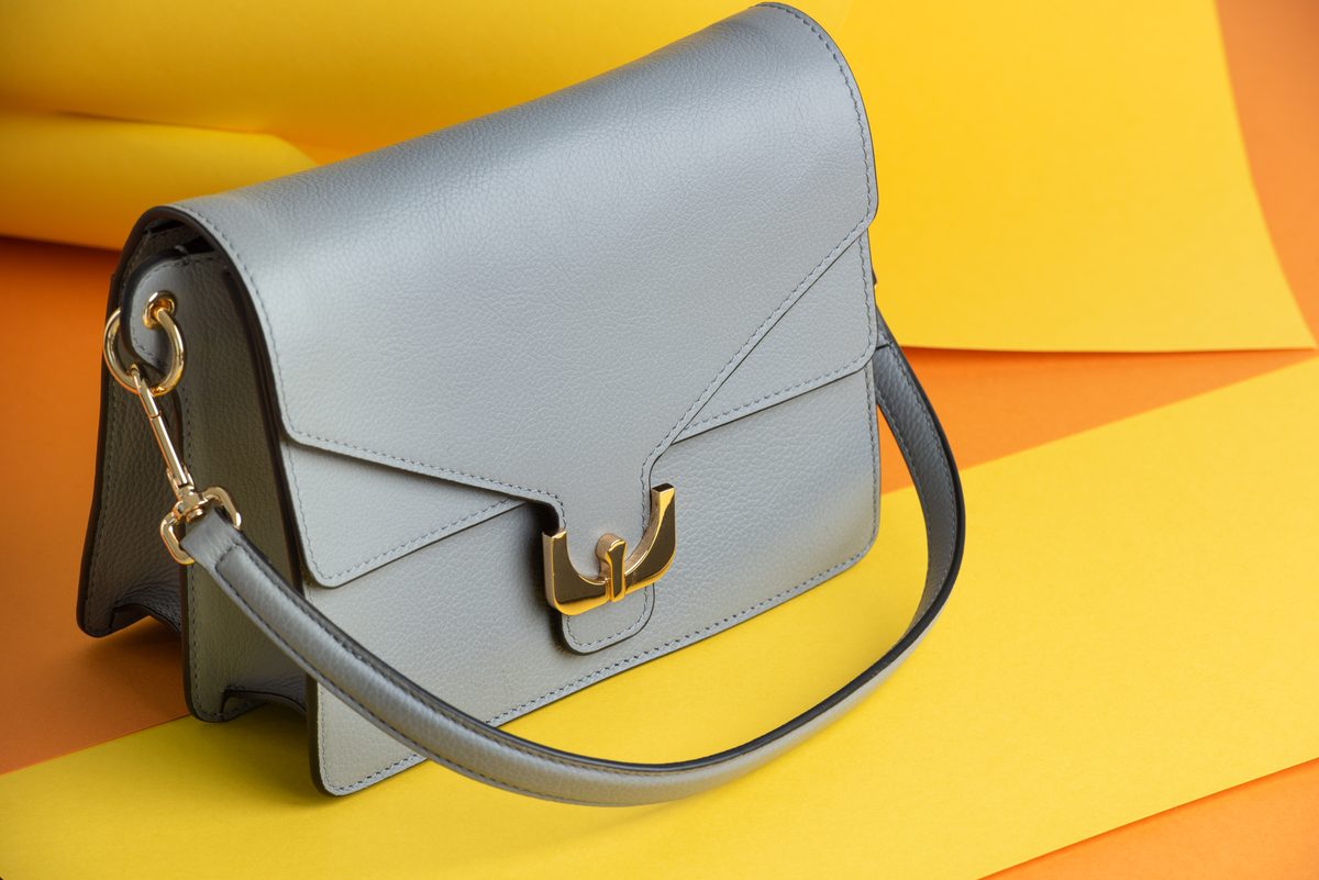 Hellgraue Ledertasche mit goldenem Verschluss vor gelbem und orangem Papierhintergrund — Das Studiozwei, Werbefotograf München