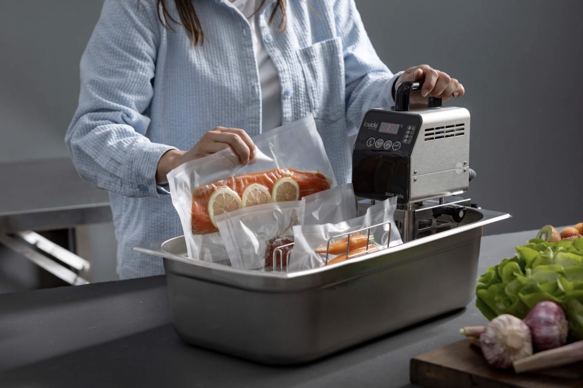 Frau legt vakuumierten Lachs in ein Wasserbad mit Sous-vide-Stick — Das Studiozwei, Werbefotograf München