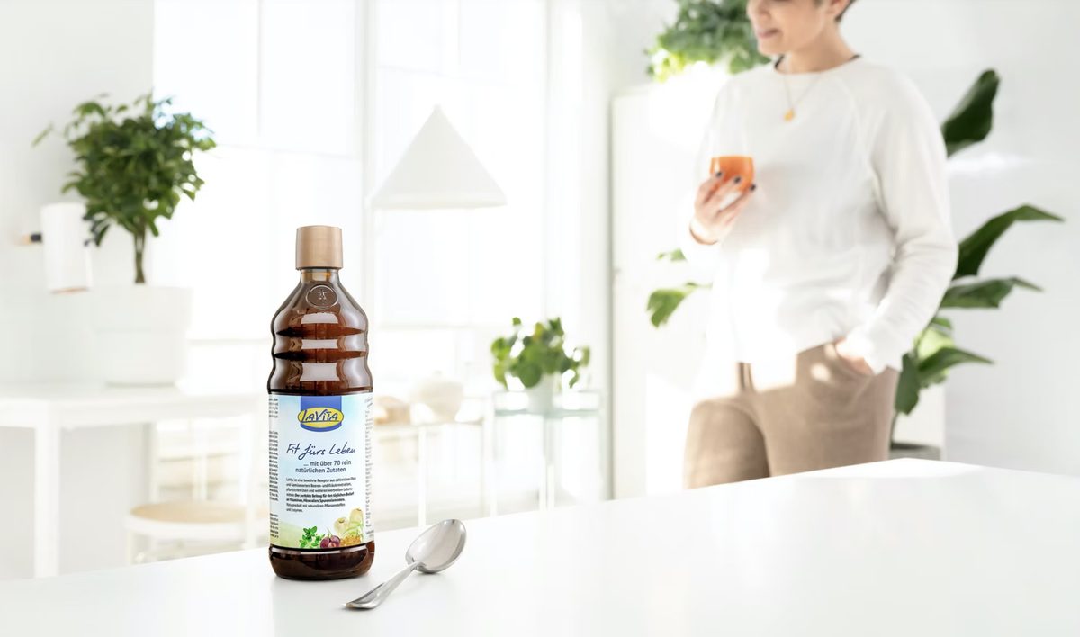 LaVita Flasche mit Loeffel auf weisser Tischplatte, im Hintergrund unscharf eine Frau — Das Studiozwei, Werbefotograf München