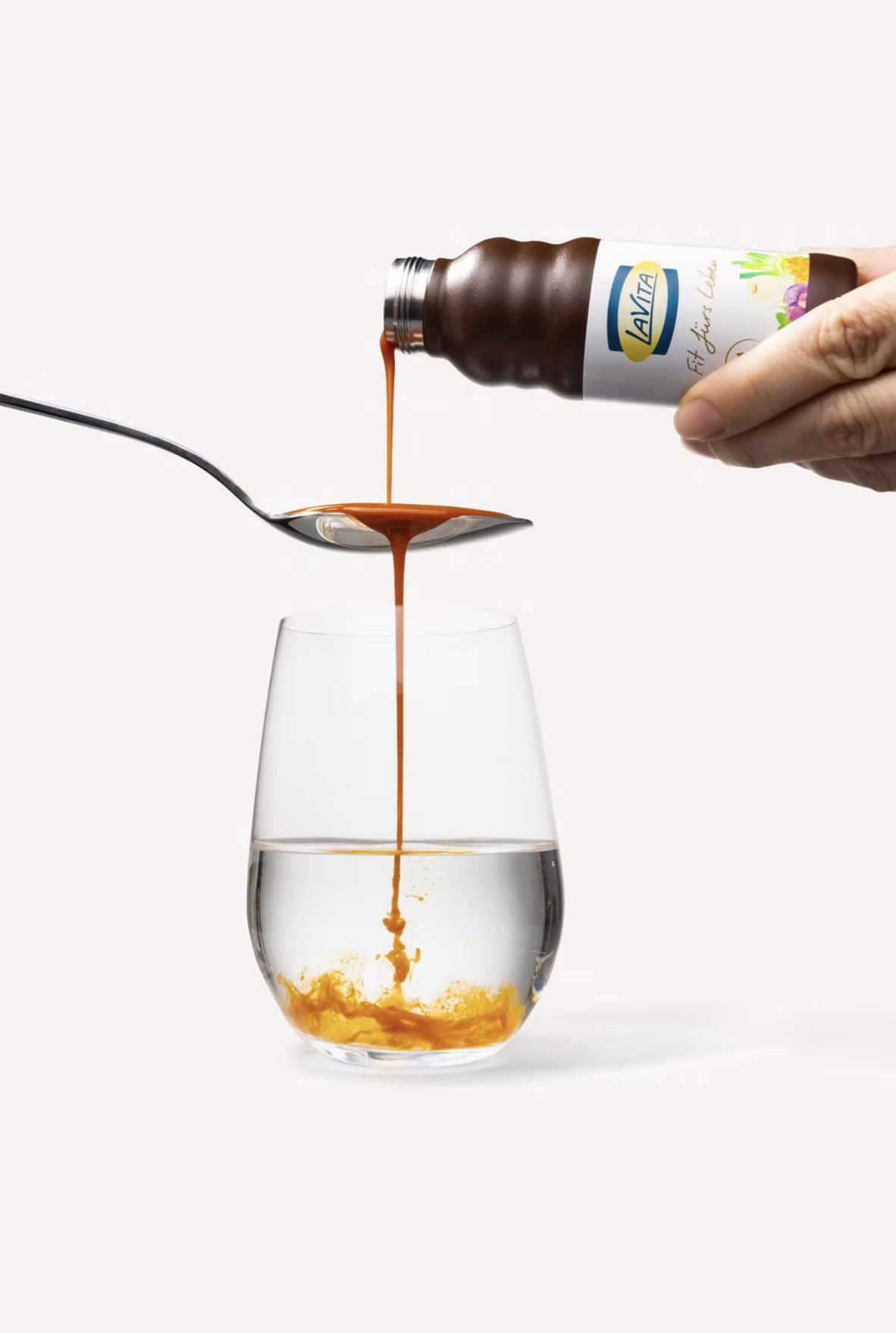Fluessiges Konzentrat laeuft von einem Loeffel in ein Wasserglas, gehalten aus der LaVita Flasche — Das Studiozwei, Werbefotograf München